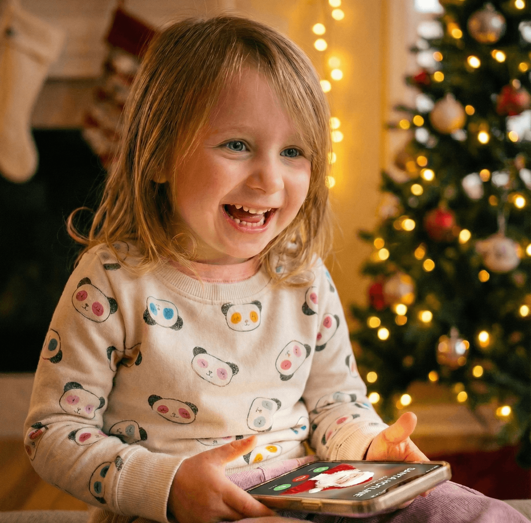 A little girl laughing with delight while talking to Santa on the phone, Christmas tree glowing in the background